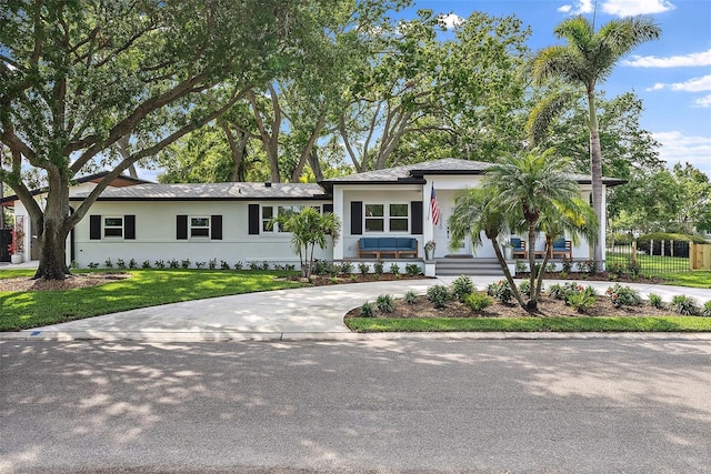 view of front of property with a front yard, curved driveway, stucco siding, and fence