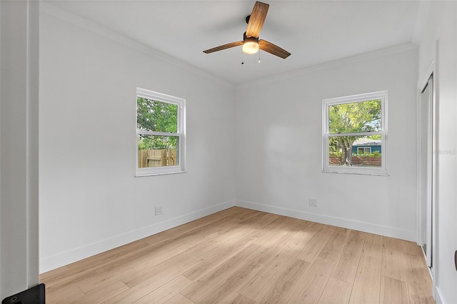 spare room with light wood finished floors, baseboards, ornamental molding, and a ceiling fan