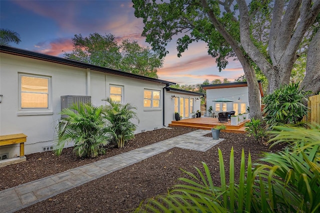 property exterior at dusk with crawl space, stucco siding, fence, and a wooden deck