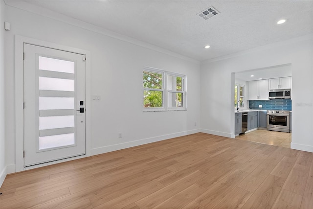 unfurnished living room with baseboards, visible vents, light wood-style flooring, and ornamental molding
