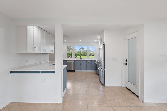 kitchen featuring white cabinetry, light countertops, stainless steel appliances, a sink, and a peninsula