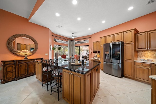 kitchen with brown cabinetry, visible vents, a kitchen breakfast bar, stainless steel fridge, and a center island