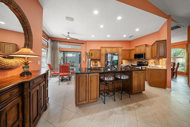 kitchen featuring a breakfast bar, backsplash, brown cabinetry, and appliances with stainless steel finishes