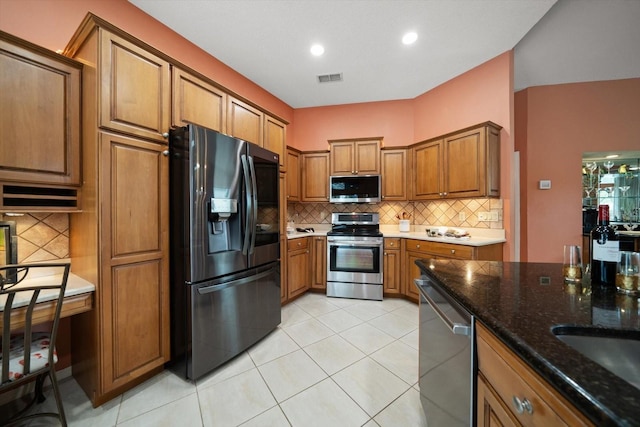 kitchen with brown cabinetry, visible vents, dark stone counters, decorative backsplash, and appliances with stainless steel finishes