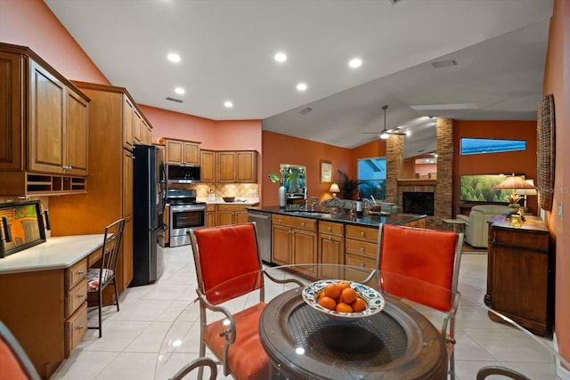 kitchen featuring light tile patterned floors, a ceiling fan, a sink, appliances with stainless steel finishes, and a brick fireplace