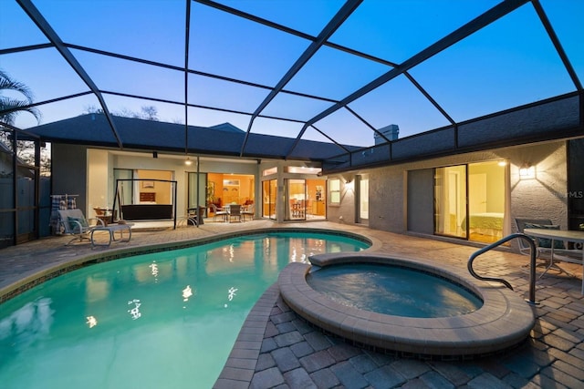 pool at dusk with glass enclosure, a patio area, and a pool with connected hot tub