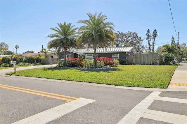 view of front facade featuring a front lawn, fence, metal roof, driveway, and a standing seam roof