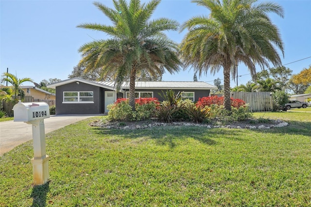 view of front facade featuring driveway, metal roof, a front yard, and fence