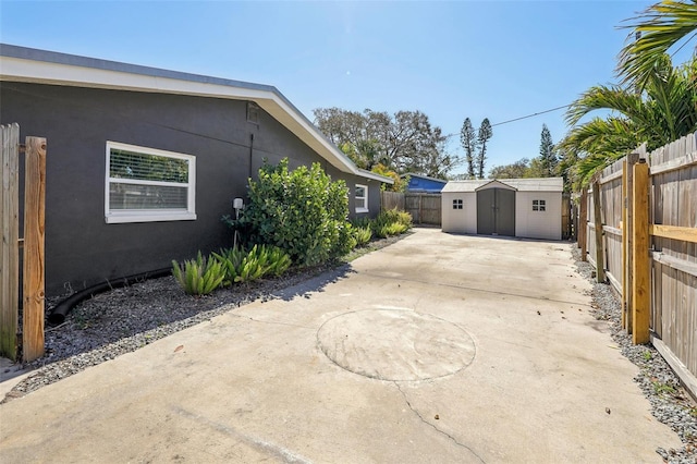 view of patio featuring a fenced backyard, a shed, driveway, and an outdoor structure