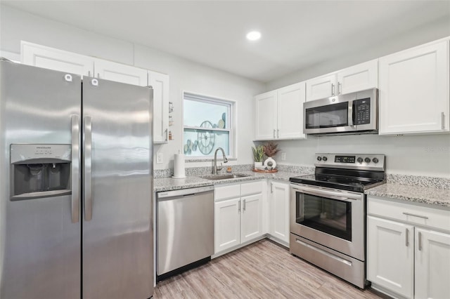 kitchen with light wood finished floors, appliances with stainless steel finishes, white cabinetry, and a sink