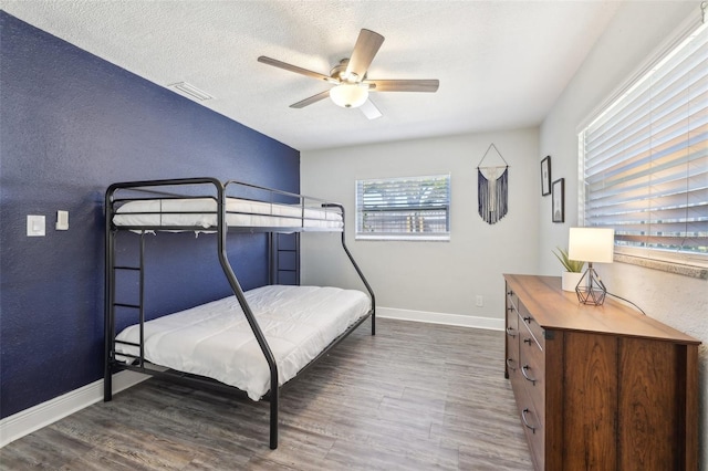 bedroom with visible vents, a textured ceiling, baseboards, and wood finished floors