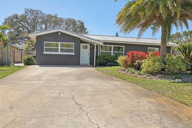 ranch-style home with stucco siding, metal roof, driveway, and fence