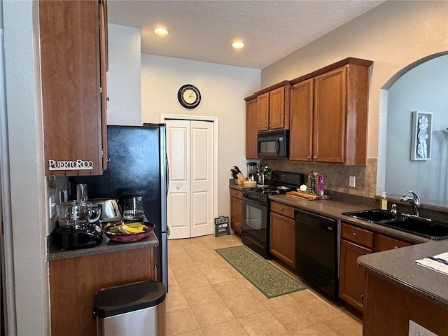 kitchen with arched walkways, a sink, black appliances, dark countertops, and brown cabinets