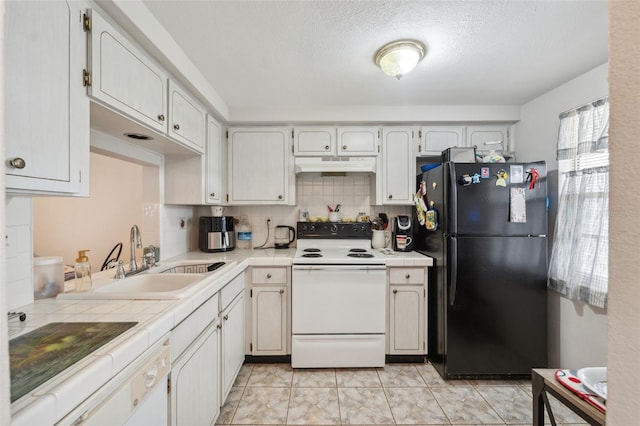 kitchen with tile countertops, white electric stove, freestanding refrigerator, a sink, and under cabinet range hood