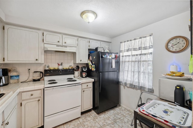 kitchen with tile countertops, white electric stove, freestanding refrigerator, decorative backsplash, and under cabinet range hood