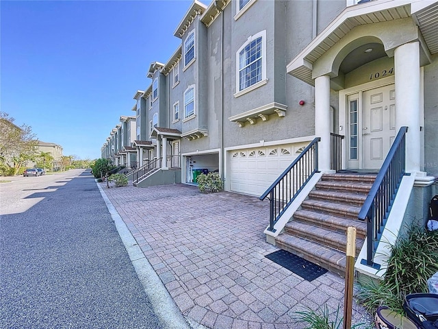 exterior space featuring an attached garage, a residential view, driveway, and stucco siding