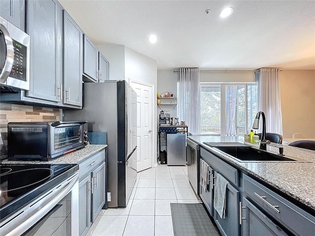 kitchen with backsplash, gray cabinetry, light tile patterned floors, stainless steel appliances, and a sink