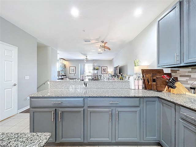 kitchen with gray cabinetry, light stone countertops, light tile patterned floors, a peninsula, and a ceiling fan