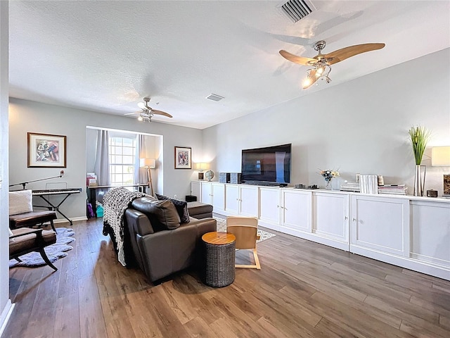 living room featuring visible vents, a textured ceiling, ceiling fan, and wood finished floors