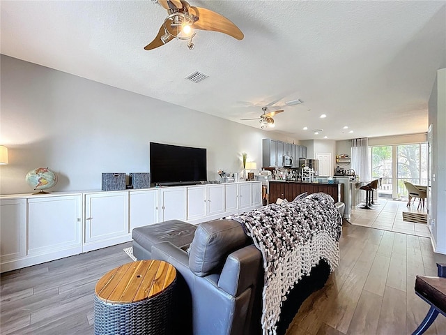 living area with light wood-style flooring, a ceiling fan, visible vents, and a textured ceiling