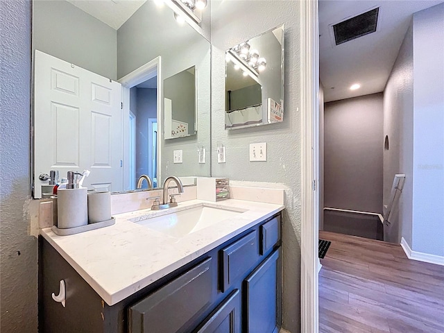 bathroom with vanity, wood finished floors, visible vents, baseboards, and a textured wall