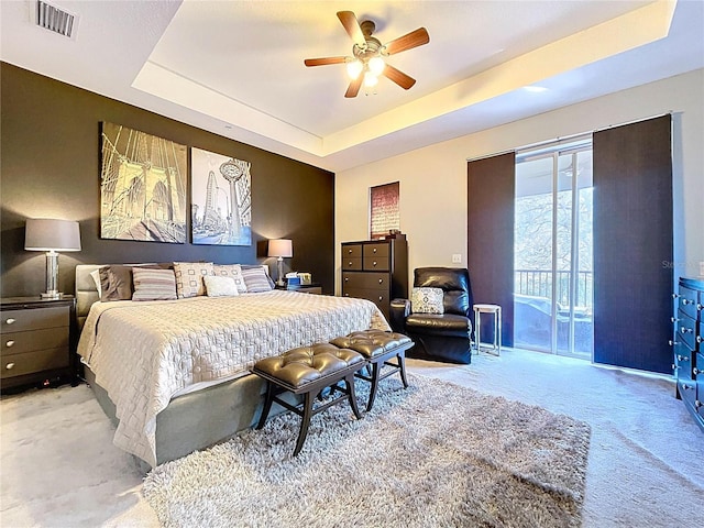 bedroom featuring access to exterior, visible vents, a tray ceiling, light carpet, and a ceiling fan