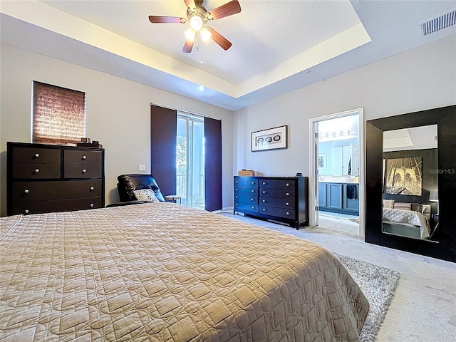 bedroom with a tray ceiling, visible vents, carpet floors, and ensuite bath