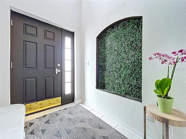 entrance foyer featuring light tile patterned flooring, a textured wall, and baseboards