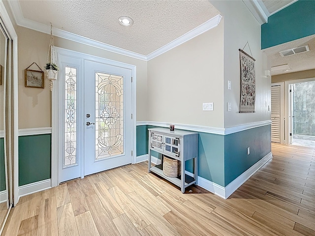 foyer featuring a textured ceiling, wood finished floors, visible vents, and ornamental molding