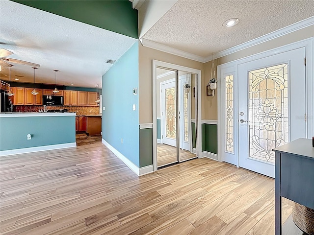 foyer featuring visible vents, a textured ceiling, crown molding, and light wood-style floors