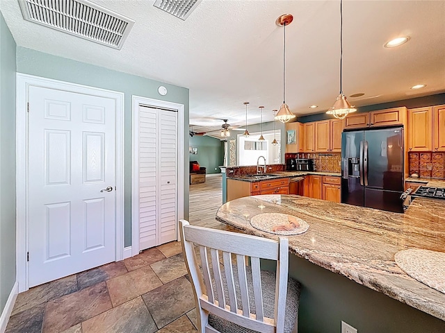 kitchen featuring light stone countertops, visible vents, a peninsula, a sink, and black fridge with ice dispenser