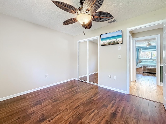 unfurnished bedroom featuring dark wood finished floors, visible vents, a textured ceiling, and a closet