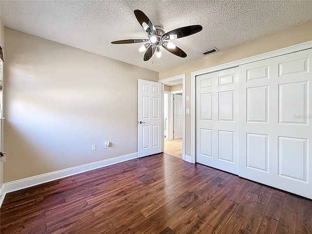 unfurnished bedroom featuring baseboards, dark wood-style floors, visible vents, and a textured ceiling