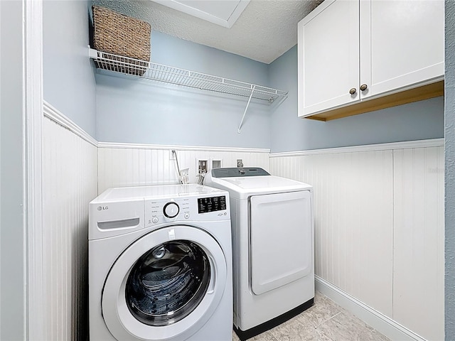 laundry room featuring cabinet space, a textured ceiling, wainscoting, and washing machine and clothes dryer