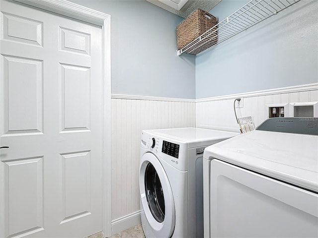 clothes washing area featuring a wainscoted wall, independent washer and dryer, and laundry area