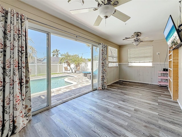 doorway to outside with ceiling fan, wood finished floors, and wainscoting