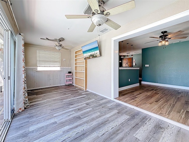 unfurnished room with a wainscoted wall, wood finished floors, visible vents, and ceiling fan