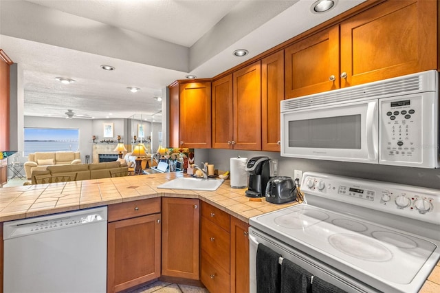 kitchen featuring open floor plan, tile countertops, a peninsula, white appliances, and a sink