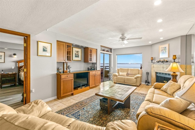 living room featuring light tile patterned floors, baseboards, a fireplace, ceiling fan, and a textured ceiling