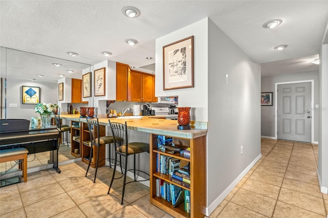 kitchen with baseboards, a breakfast bar area, light countertops, brown cabinets, and a peninsula