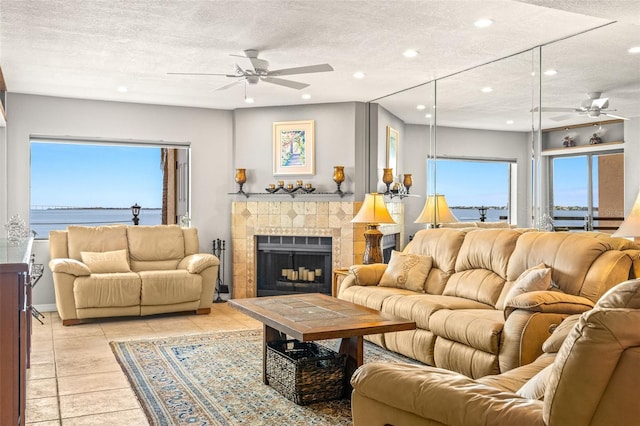 living area with a ceiling fan, light tile patterned flooring, recessed lighting, a tile fireplace, and a textured ceiling