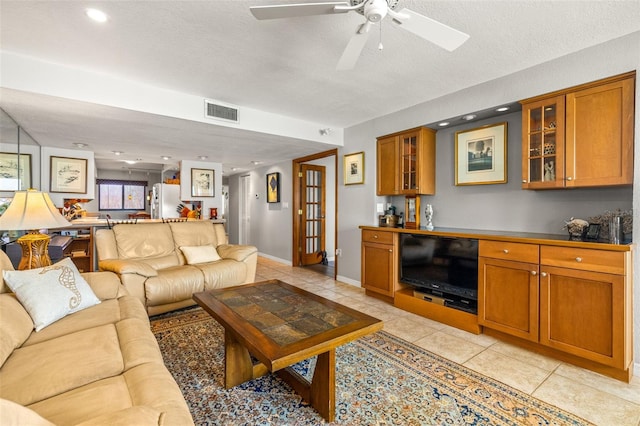 living room with light tile patterned flooring, a ceiling fan, visible vents, and a textured ceiling