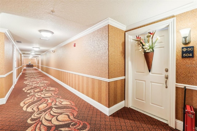 hallway featuring visible vents, wallpapered walls, crown molding, carpet flooring, and a textured ceiling