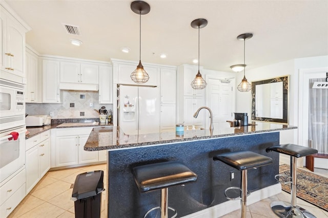 kitchen featuring white appliances, light tile patterned floors, visible vents, white cabinetry, and a kitchen breakfast bar