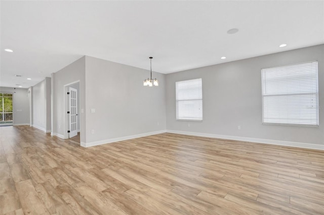 spare room with an inviting chandelier, light wood-style flooring, recessed lighting, and baseboards