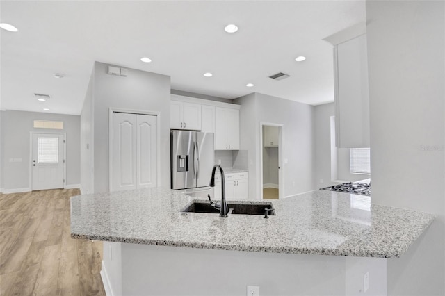 kitchen featuring visible vents, a sink, white cabinetry, stainless steel fridge, and a peninsula