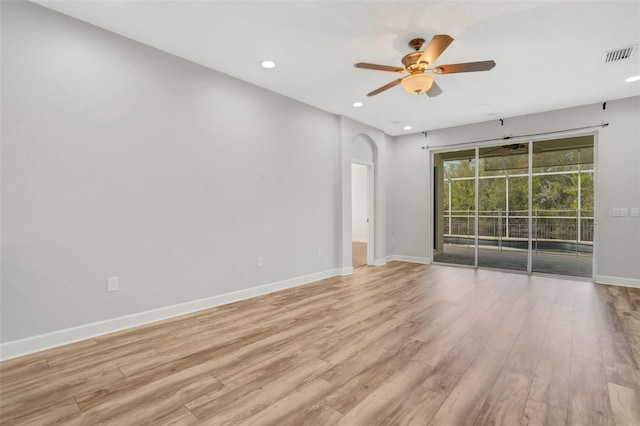 spare room featuring visible vents, light wood-style flooring, a ceiling fan, arched walkways, and baseboards