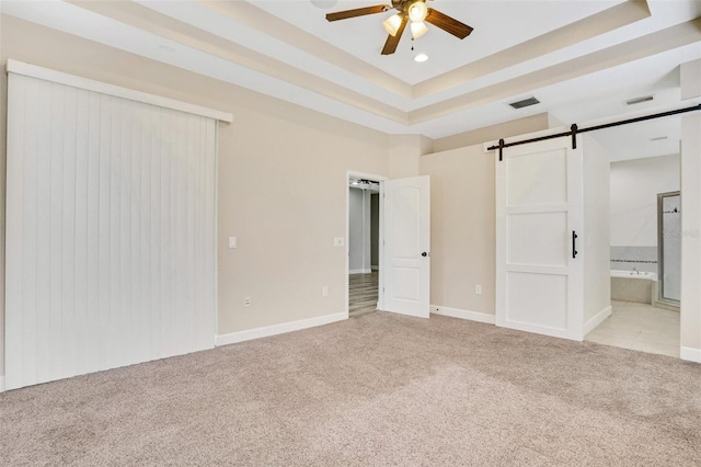 unfurnished bedroom with visible vents, a tray ceiling, ensuite bathroom, light carpet, and a barn door