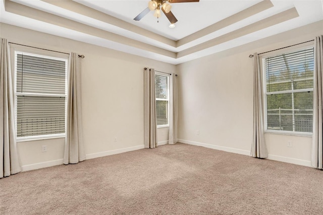 carpeted spare room featuring baseboards, a raised ceiling, and a ceiling fan