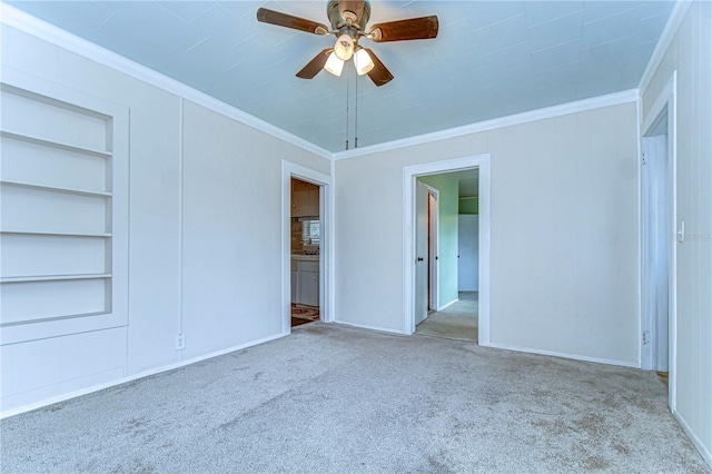 carpeted spare room featuring baseboards, built in shelves, ceiling fan, and crown molding